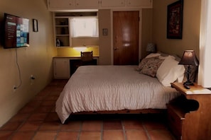 Un dormitorio con cama, escritorio, silla, televisor y puerta.