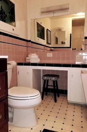 Un baño con inodoro, lavabo, espejo y un taburete pequeño.