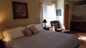 A bedroom with a large bed, a chair, a nightstand, a lamp, and a painting on the wall.