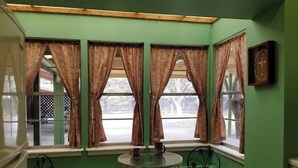 A room with green walls, three windows with curtains, a round table with two chairs, and a picture on the wall.