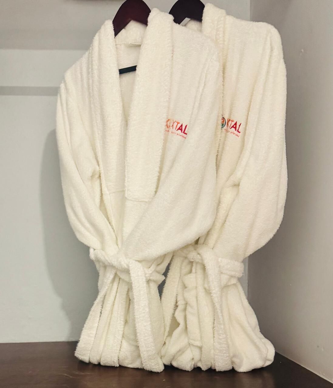 Two white bathrobes with red text hanging on a wooden hanger.