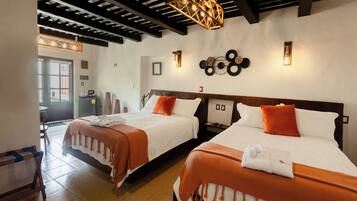 A hotel room with two beds, each with white linens and orange accents, a wooden headboard, and a ceiling with exposed beams.