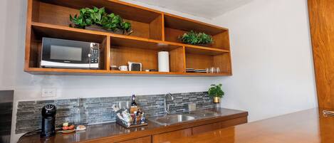 Una cocina moderna con armarios de madera, microondas integrado, un fregadero y un estante con plantas.