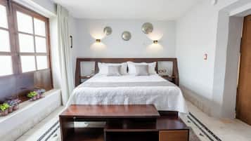 Ein Schlafzimmer mit einem großen Bett, Nachttischen, einer hölzernen Bank, einem Fenster mit Vorhängen und Wandleuchten.