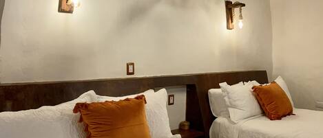 A hotel room with two beds, each with white linens and a brown pillow. There are wall-mounted light fixtures and a wooden ceiling beam.
