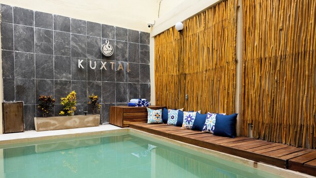A pool area with a wooden bench, a wall with a logo, and a bamboo wall. - Kuxtal Hotel Boutique (Mérida)