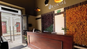 A reception desk with a wooden finish, a wall-mounted clock, and a decorative floral wall to the right. - Kuxtal Hotel Boutique (Mérida)