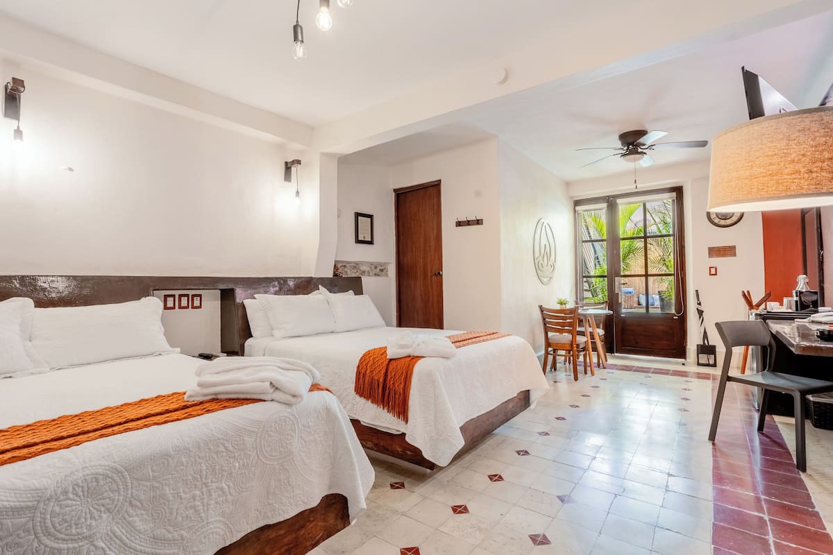 Habitación de hotel con dos camas, una zona de comedor y vistas al exterior.