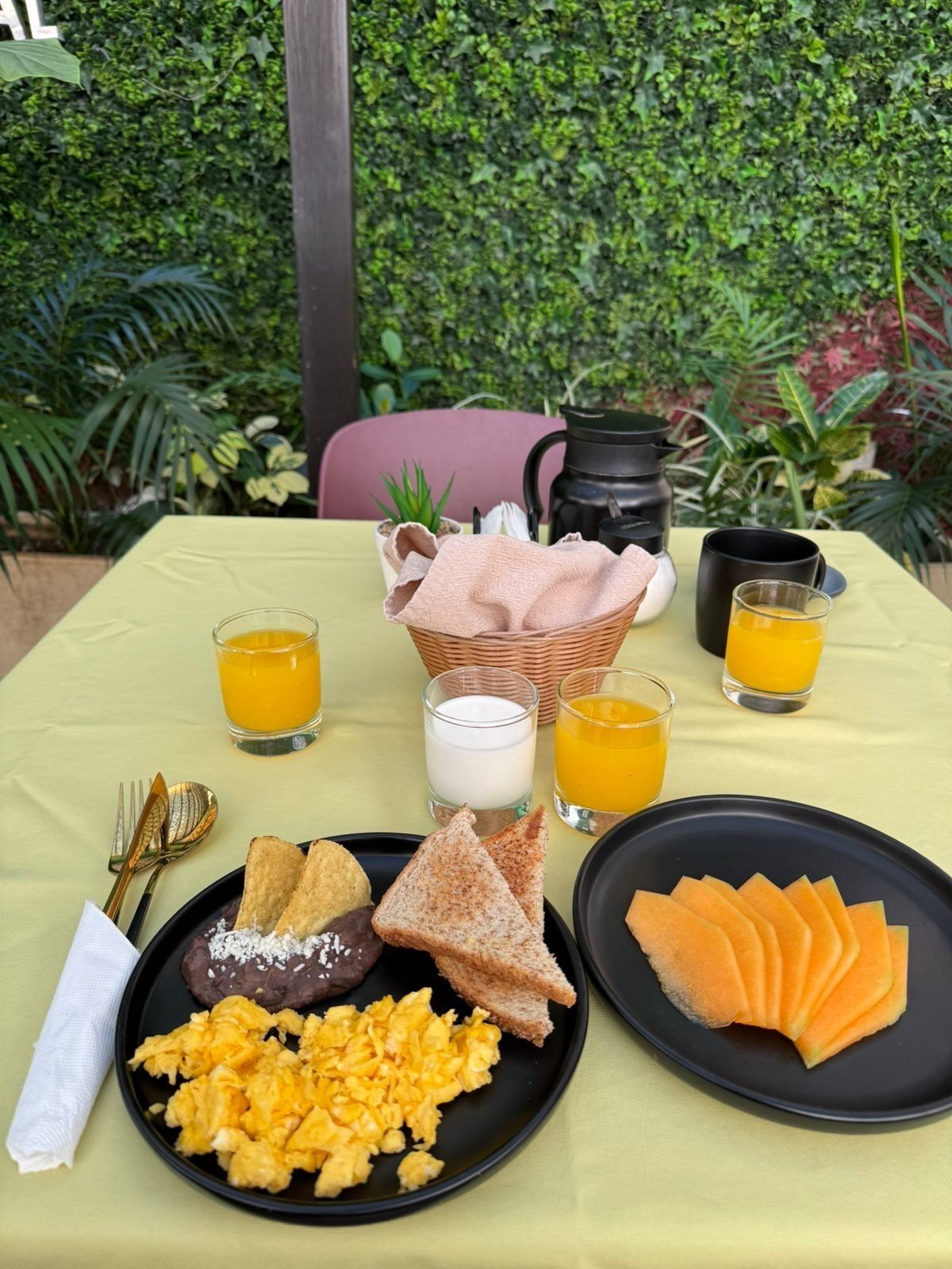A breakfast setting with toast, scrambled eggs, and fruit on plates, accompanied by drinks and a pitcher.