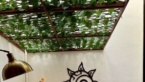 A dining area with a round table, two chairs, a wall-mounted sun decoration, a potted plant, and a pendant light. - Kuxtal Hotel Boutique (Mérida)