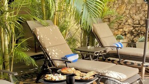 A lounge area with two sun loungers, a table with food and drinks, and a patterned floor. - Kuxtal Hotel Boutique (Mérida)