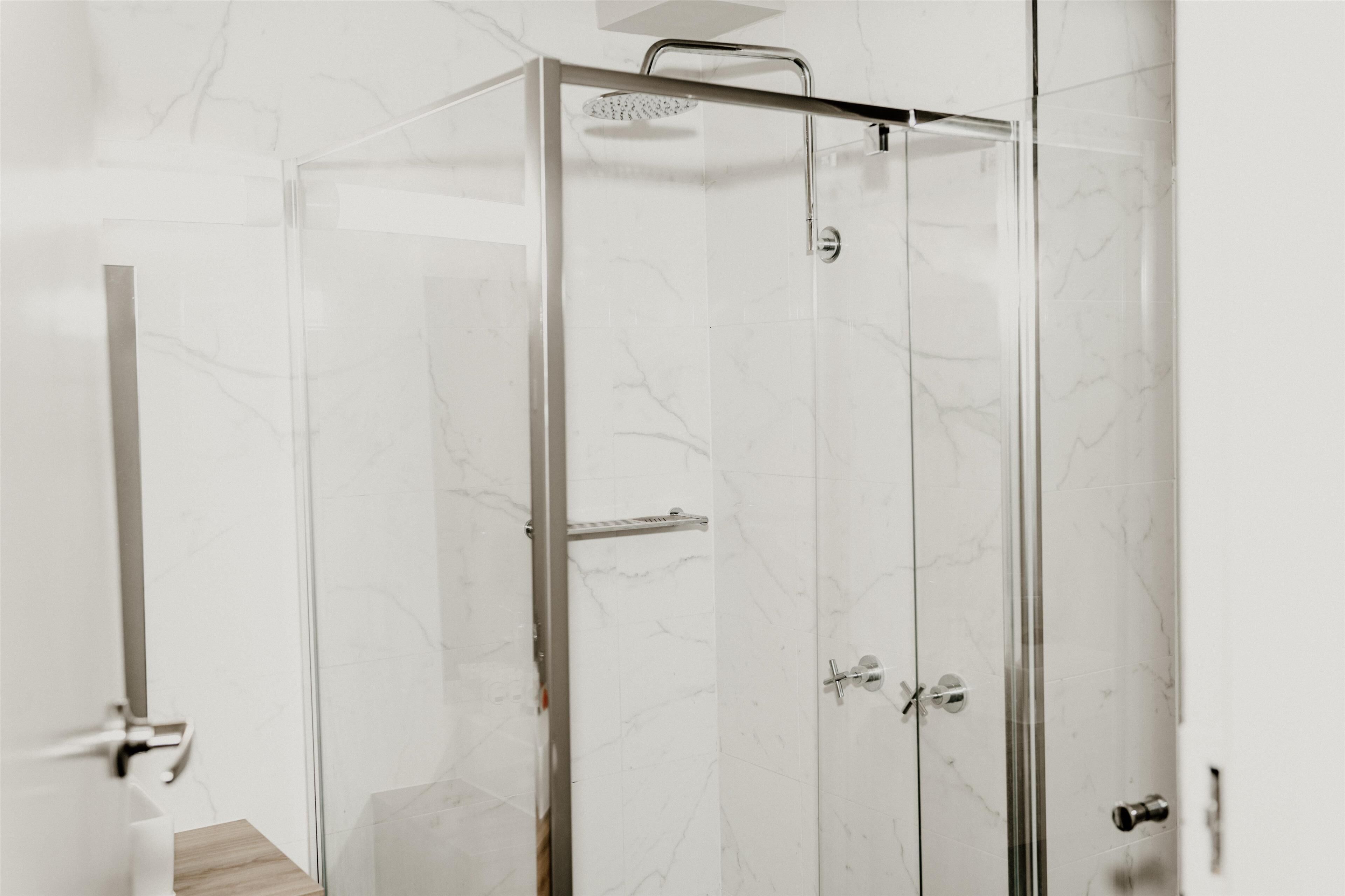Une douche fermée par des parois en verre, dotée d’un pommeau de douche à main, d’un porte-serviettes et d’une porte avec une poignée.