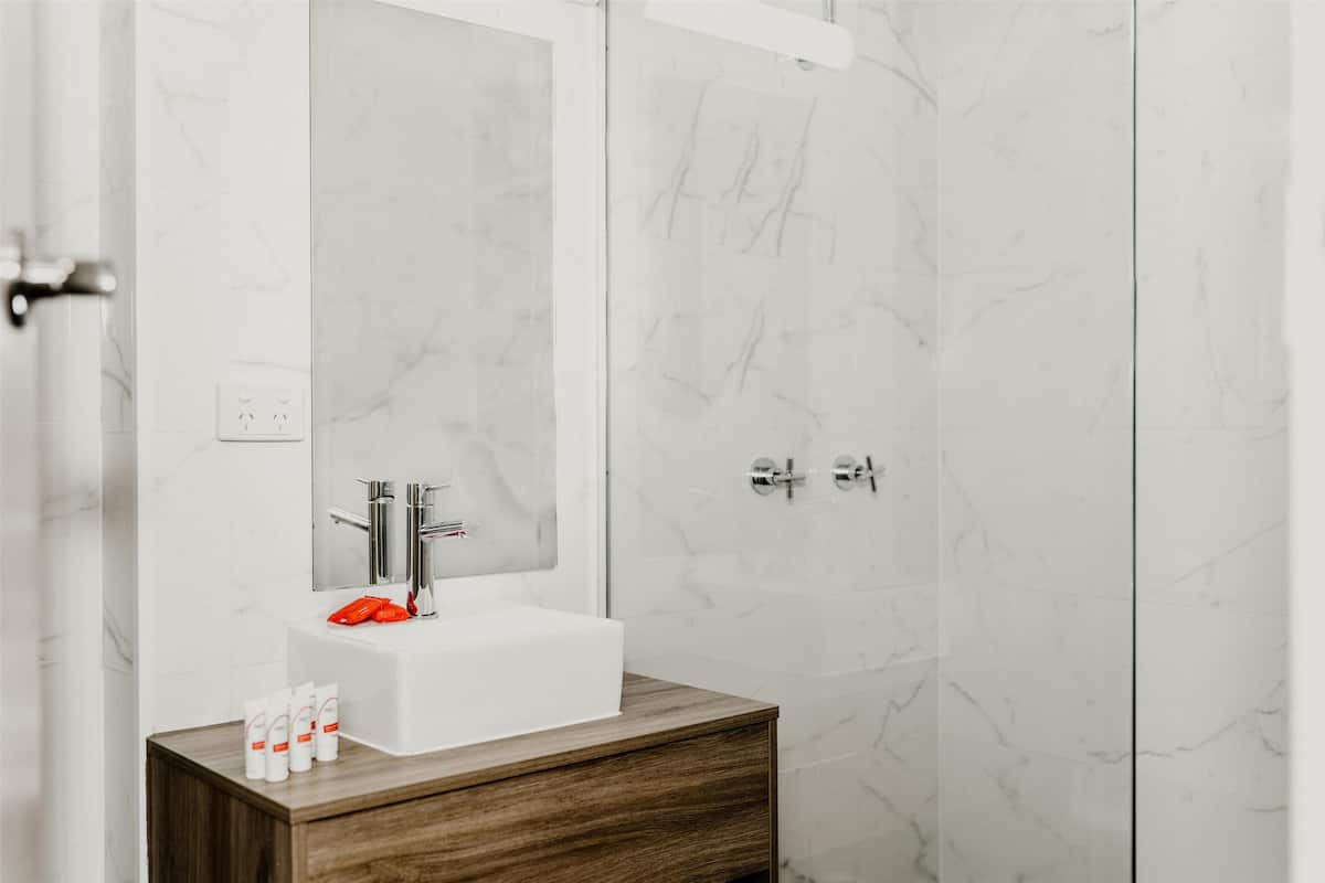 A modern bathroom with a white marble sink, wooden vanity, and a large mirror.