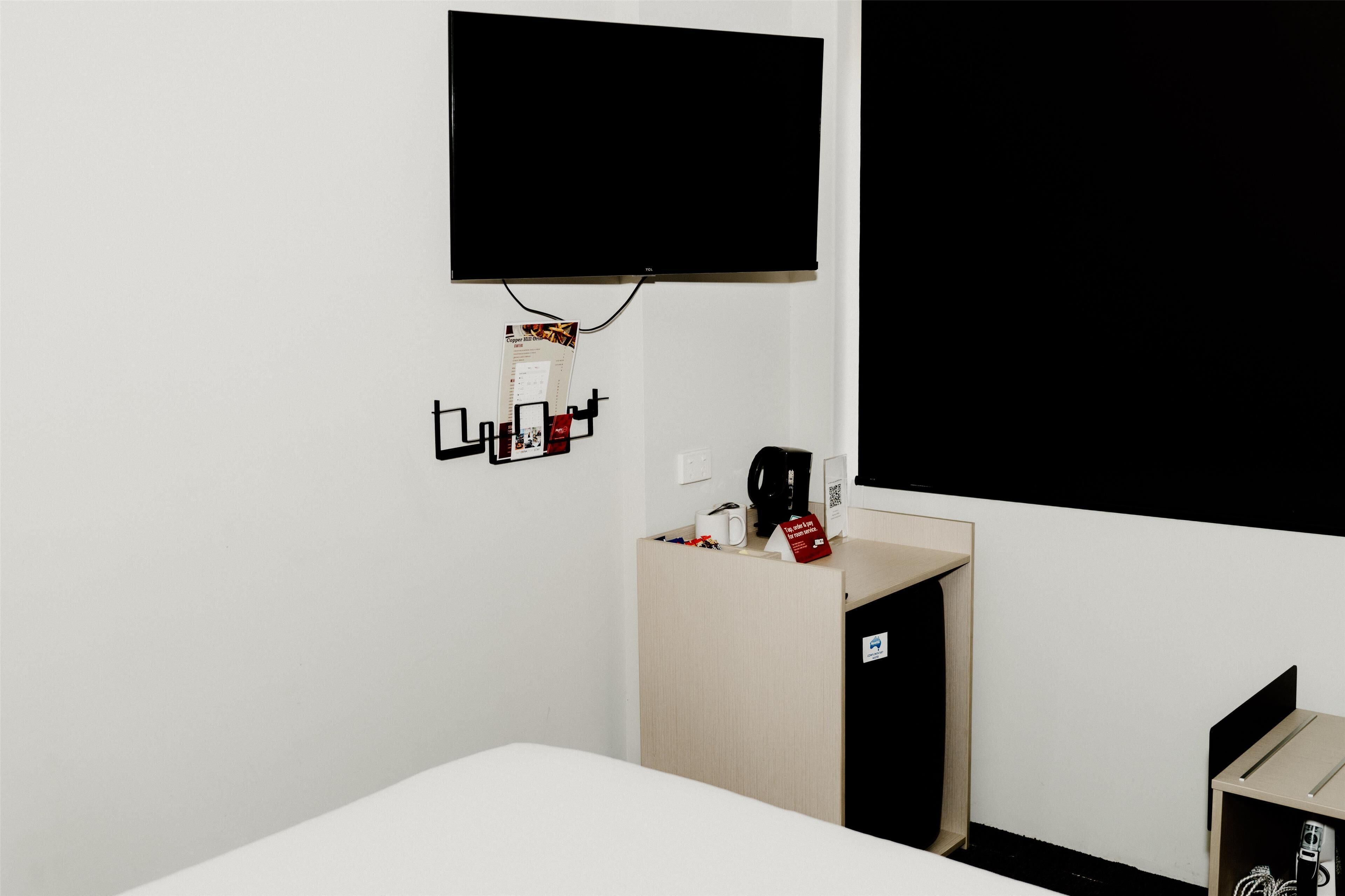 A hotel room with a bed, a small desk with a coffee machine, a TV mounted on the wall, and a wooden cabinet.