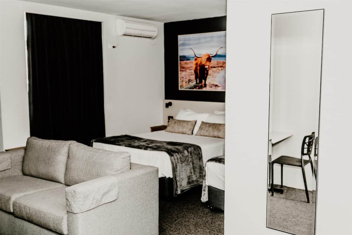 A hotel room with a bed, a sofa, a chair, and a large mirror.