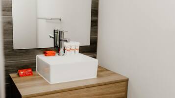 Un baño con un lavabo blanco, un espejo y un mueble de madera. Hay un secador de pelo y artículos de aseo en el lavabo.