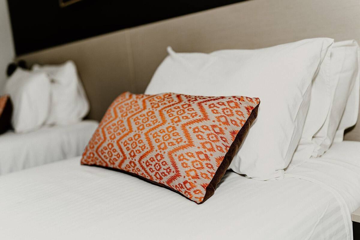 A hotel room with a bed featuring white bedding and a single orange patterned pillow.