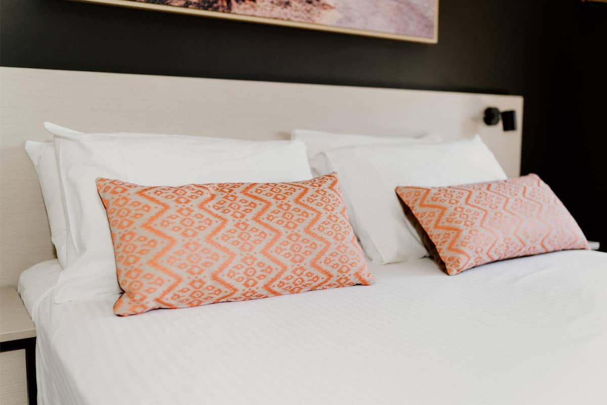 A bed with white linens and two orange patterned pillows.