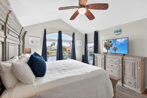 Une chambre à coucher comprenant un lit, un ventilateur de plafond, une télévision, une vue sur l’extérieur et une armoire en bois.