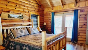 A wooden cabin bedroom with a bed, a window with curtains, and a wooden headboard.