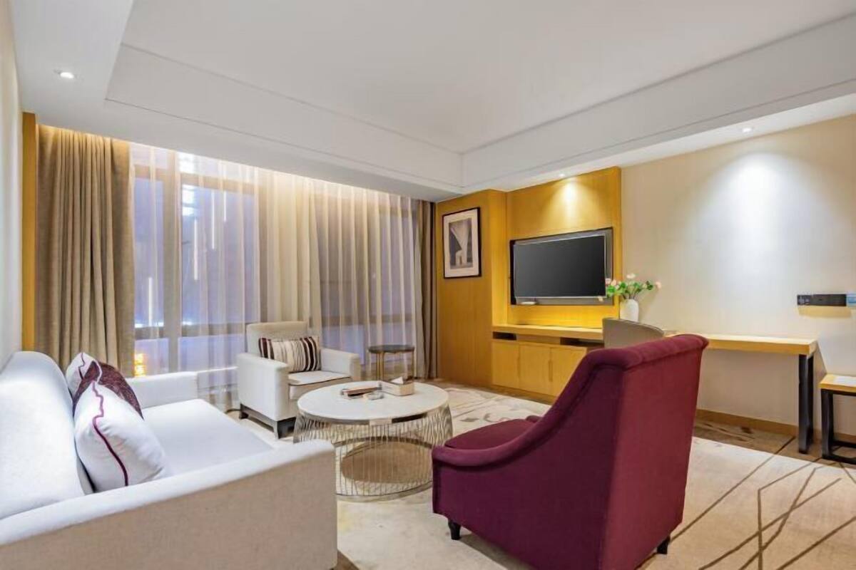 Una habitación de hotel moderna con sofá, sillón, mesa de centro redonda, televisor y escritorio.