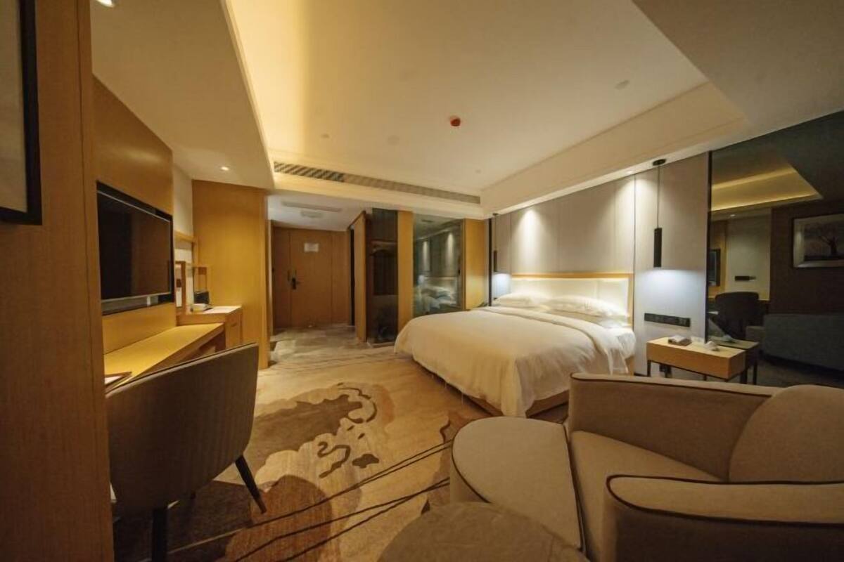 Una habitación de hotel con cama, escritorio, silla, televisor y lámpara.