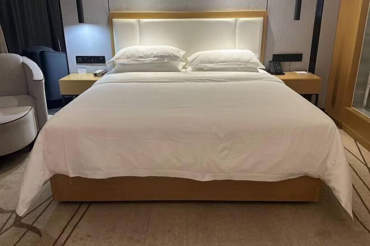 Una habitación de hotel con una cama grande, una mesita de noche con lámpara, una silla y otro aparador con teléfono.