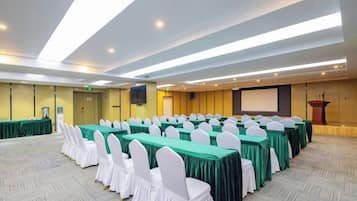 A conference room with rows of tables and chairs, a podium, and a screen.