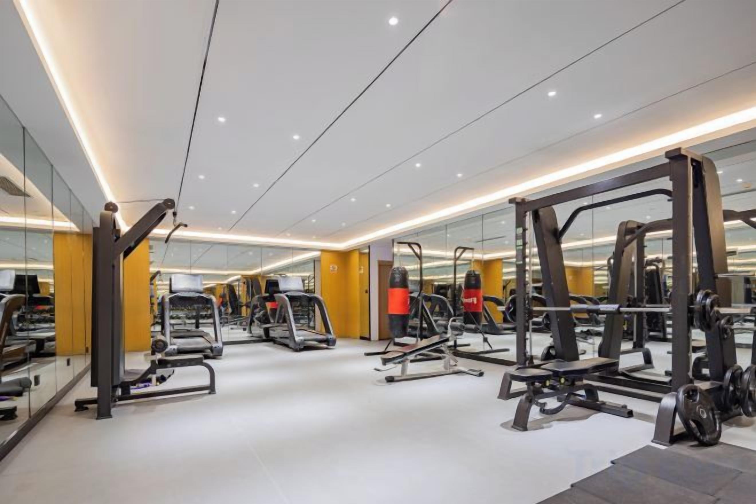 Une salle de sport moderne dotée de divers appareils d’exercice, de murs recouverts de miroirs et d’un intérieur propre et bien éclairé.