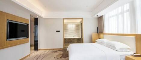Une chambre d’hôtel moderne dotée d’un grand lit, d’un téléviseur à écran plat fixé au mur, d’une table de chevet en bois et d’une salle de bain avec un lavabo en marbre.