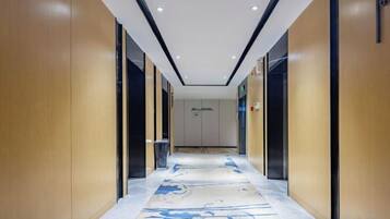 A hotel corridor with wooden walls, a carpeted floor, and a sign indicating the direction to the elevator.