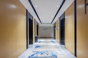 Pasillo de hotel con paredes de madera, piso alfombrado y un cartel que indica la dirección al ascensor.