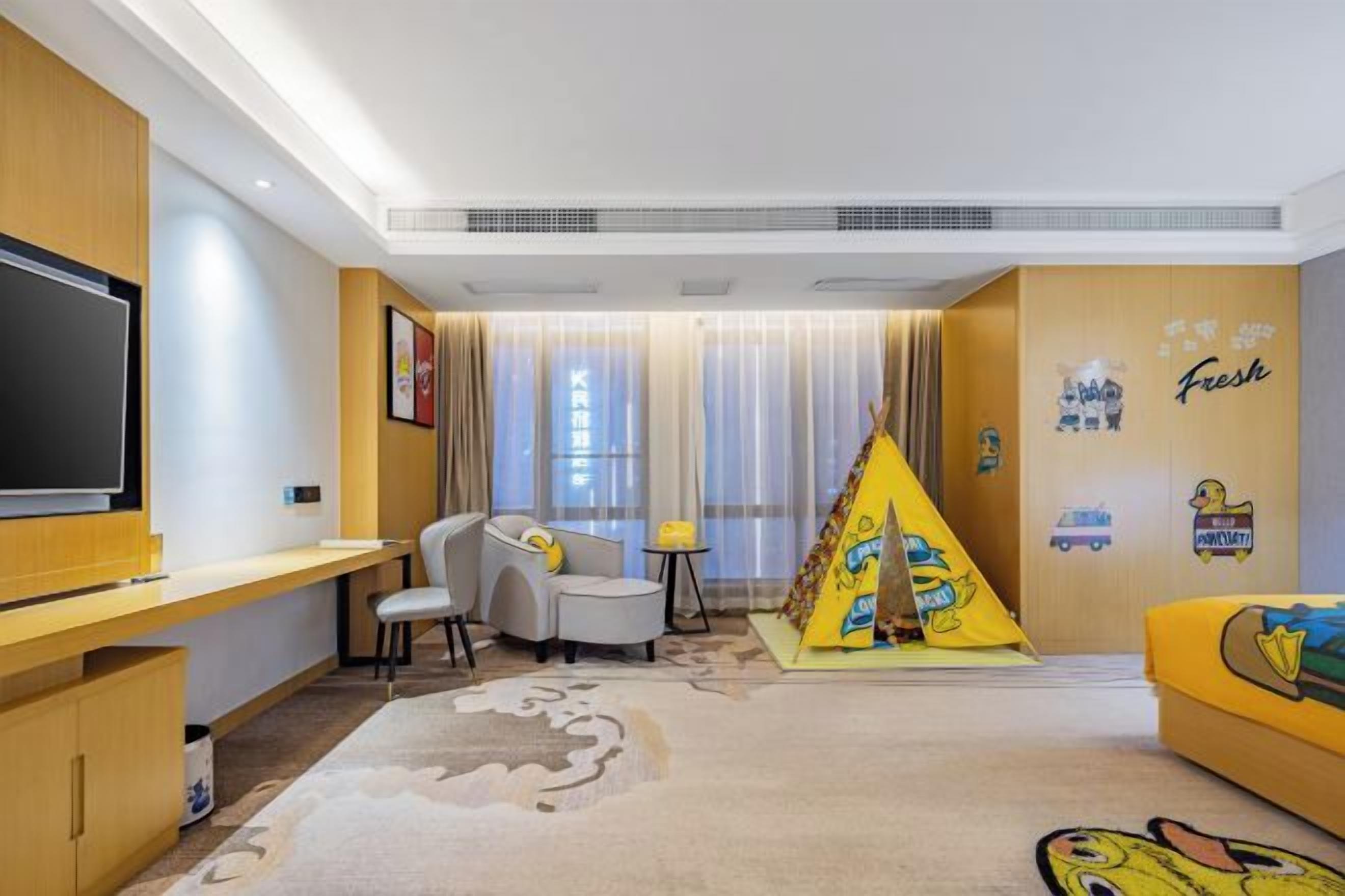 Habitación de hotel con televisión de pantalla plana, escritorio, silla, sofá, mesita pequeña y decoración en la pared.