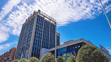 Un edificio de varios pisos con fachada moderna de vidrio, rodeado de árboles y bajo un cielo parcialmente nublado.