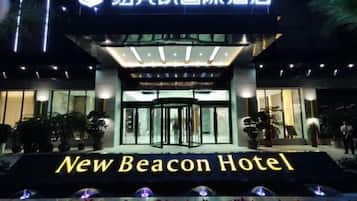 Exterior del Hotel New Beacon, con una entrada destacada, fachada de vidrio y un letrero con el nombre del hotel.