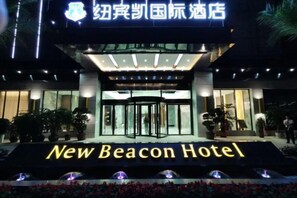 The exterior of the New Beacon Hotel with a prominent entrance, a glass facade, and a sign indicating the hotel's name. - New Beacon International Hotel (Enshi Cultural Center) (Enshi City)