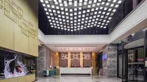 En modern hotellobby med en receptionsdisk, marmorgolv och en geometrisk takdesign.
