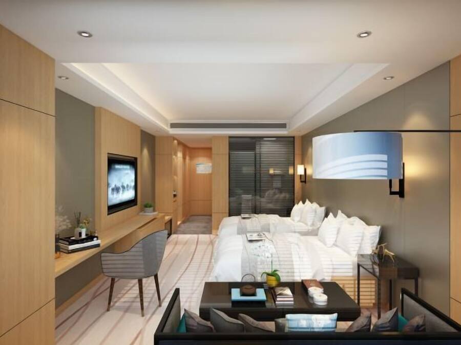 A modern hotel room with a bed, a desk, a chair, a TV, and a lamp.
