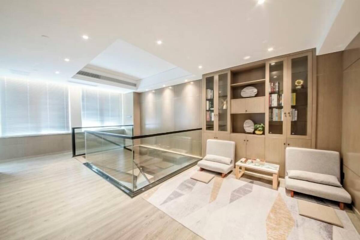 Una sala de estar moderna con barandilla de cristal, dos sillones, una mesa de centro y estanterías empotradas con libros y objetos decorativos.
