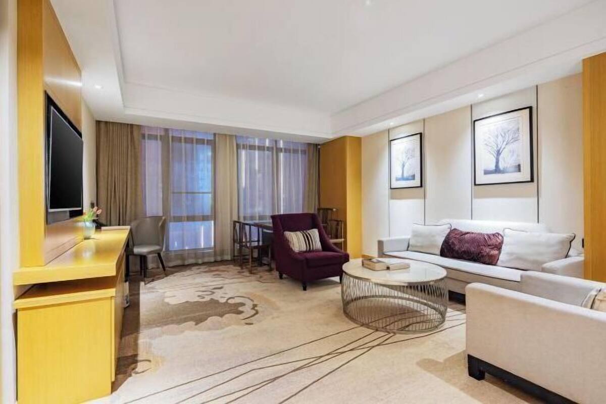 Una habitación de hotel moderna con sofá, sillones, una mesa de centro, televisión y escritorio.