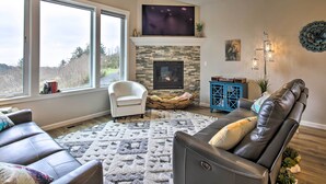 A living room with a fireplace, a television, and a large window. - Stunning Neskowin Gem: View of Cascade Head! (Neskowin)