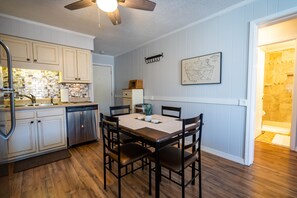 A kitchen with wooden cabinets, a dining table with chairs, a ceiling fan, and a map on the wall. - Steps From The Beach! 2BR Modern Family Condo! (Myrtle Beach)