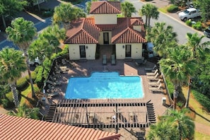 A two-story building with a swimming pool, surrounded by palm trees and lounge chairs.
