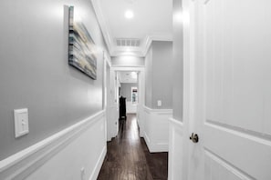 A hallway with white walls, a dark wooden floor, and a door on the right.