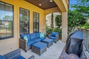 A covered outdoor seating area with wicker furniture and a grill.