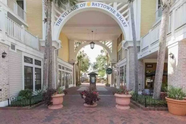 A covered walkway with a sign reading 'The Village of Baytowne Wharf' leading to a building with a coffee shop visible.