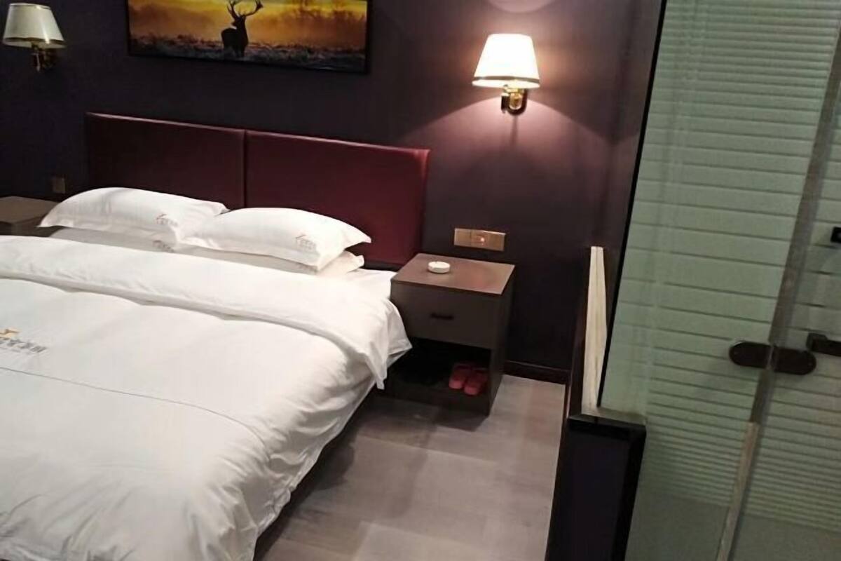 Een hotelkamer met een bed, nachtkastje, lamp en een schilderij aan de muur.