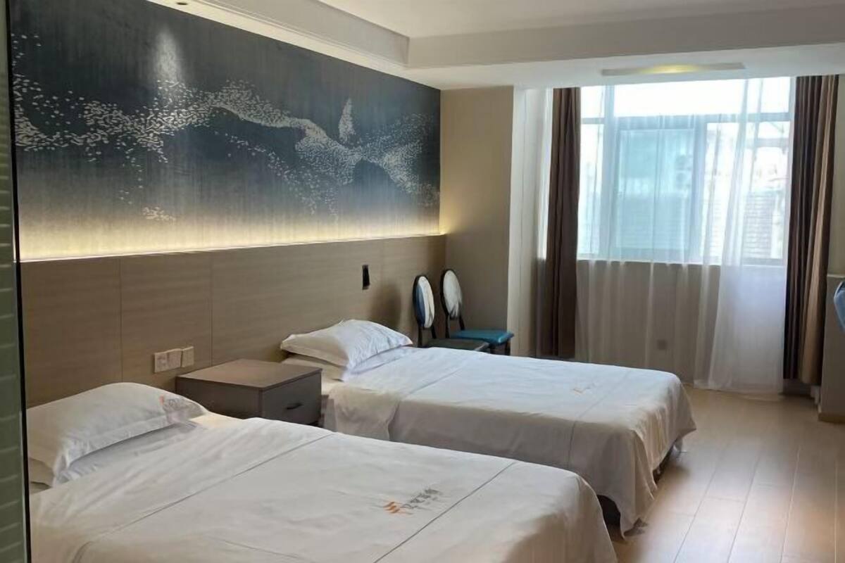 Hotelkamer met twee bedden, een groot abstract kunstwerk aan de muur, een bureau met een laptop en een groot raam met gordijnen.