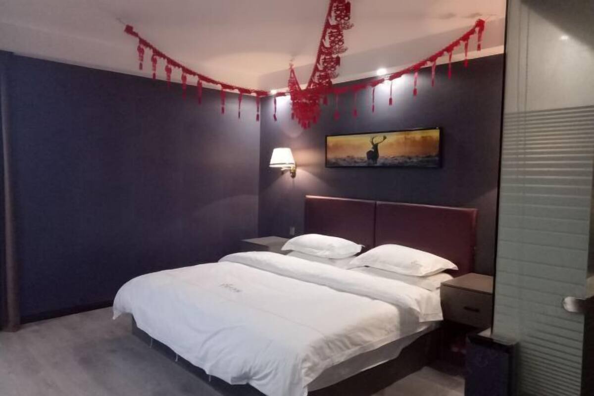 Een slaapkamer met een bed, nachtkastjes, een wandlamp en een schilderij.