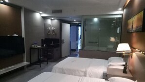 Habitación de hotel con dos camas, un escritorio, un televisor y un baño con cabina de ducha de vidrio.